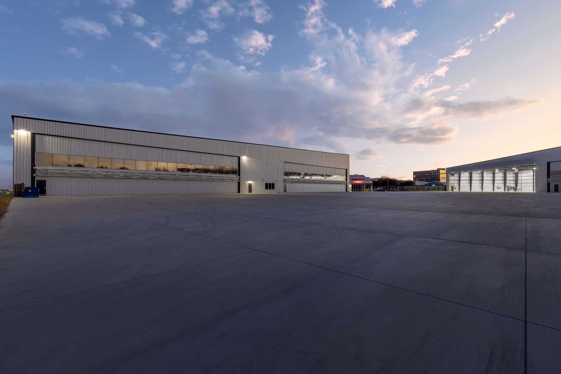 view of two buildings housing airplane hangers in San Antonio at dusk and the building in the background has the door open